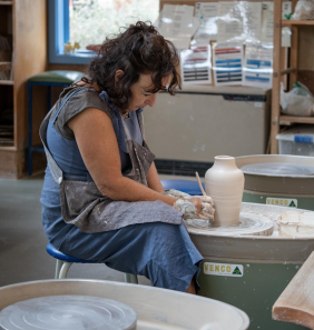 Lady with brown hair sculpting a vase at a pottery wheel 