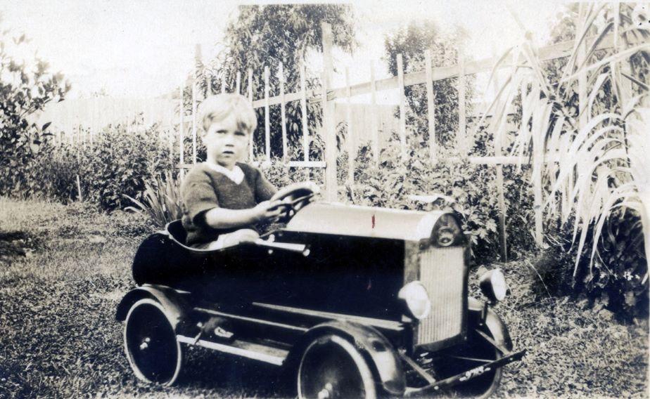 Black and white photo of a boy driving an expensive toy car