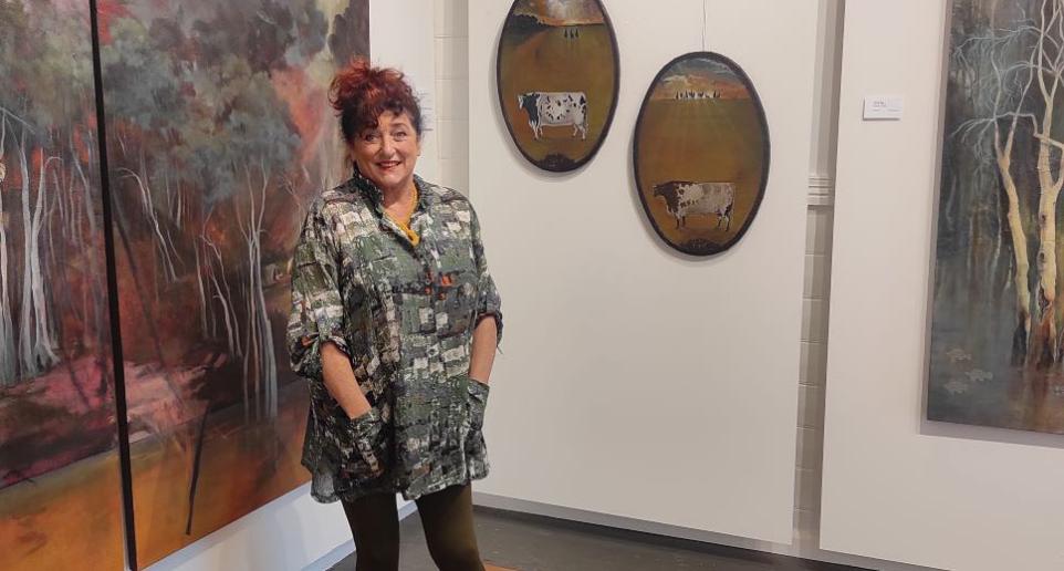 Helen S.Tiernan smiles in front of landscape paintings with cows