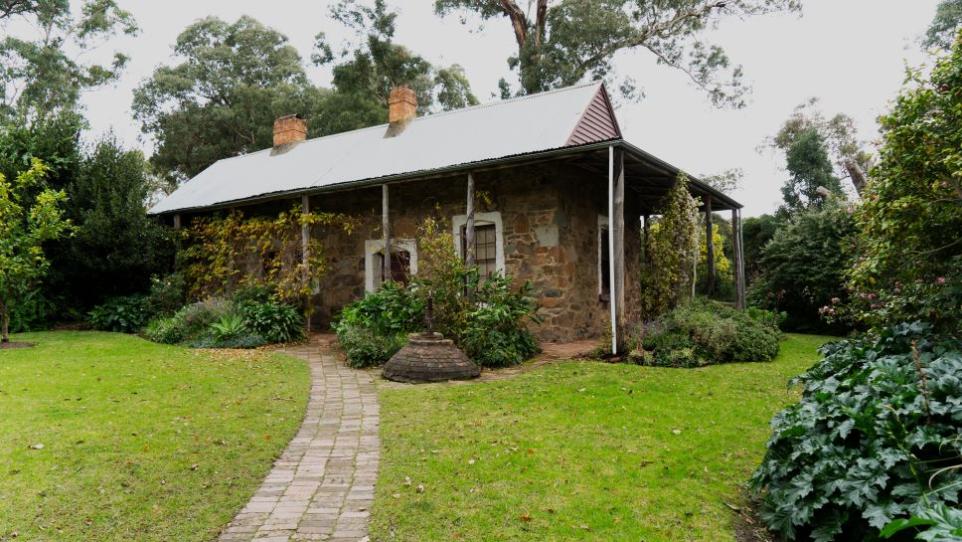 View of a pioneer stone cottage in a garden.