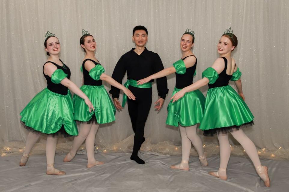 Ballet dancers posing for a photo, boy dressed in black at centre with two girls either side dressed in green.