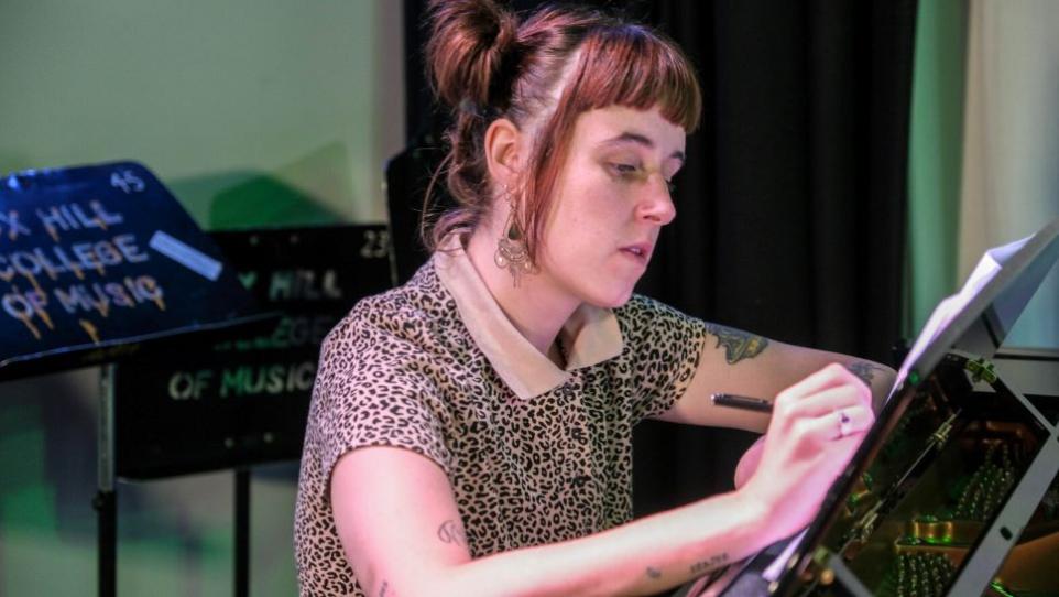 Young woman in leopard print top writing in a music studio.