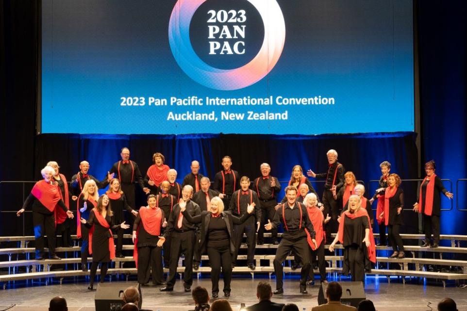 Chorus arranged on risers performing on stage, dressed in black and red.