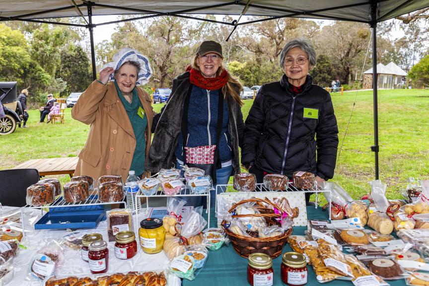 Three ladies smiling behind a cake stall