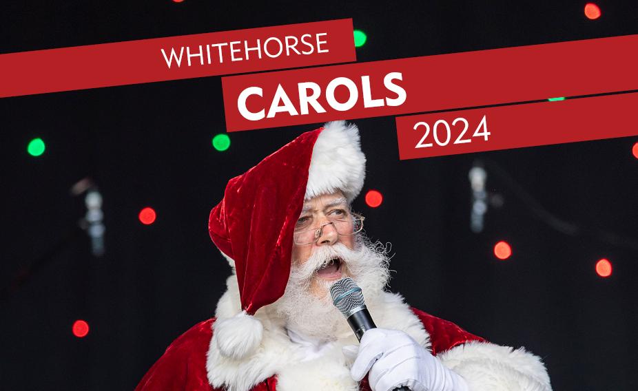 Person dressed as Santa singing into a microphone on a stage