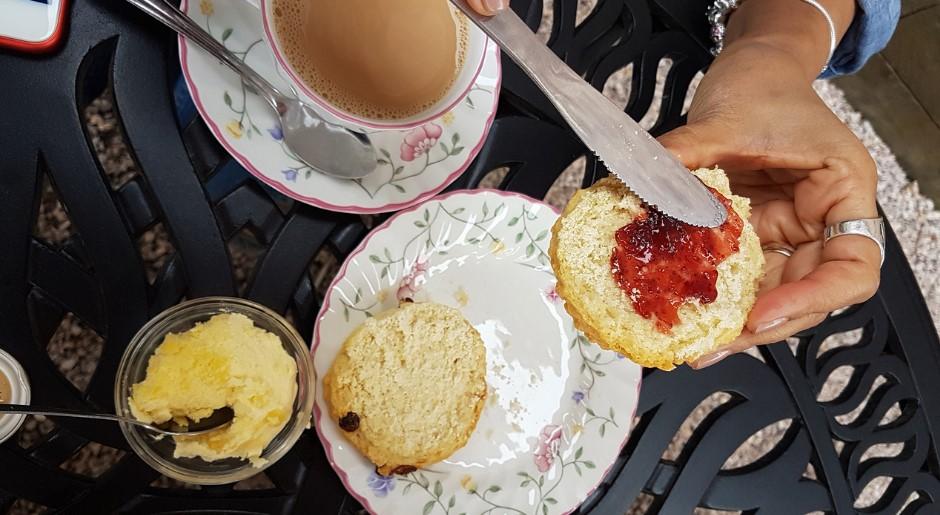 devonshire tea setting, person's hand putting Jam on scone