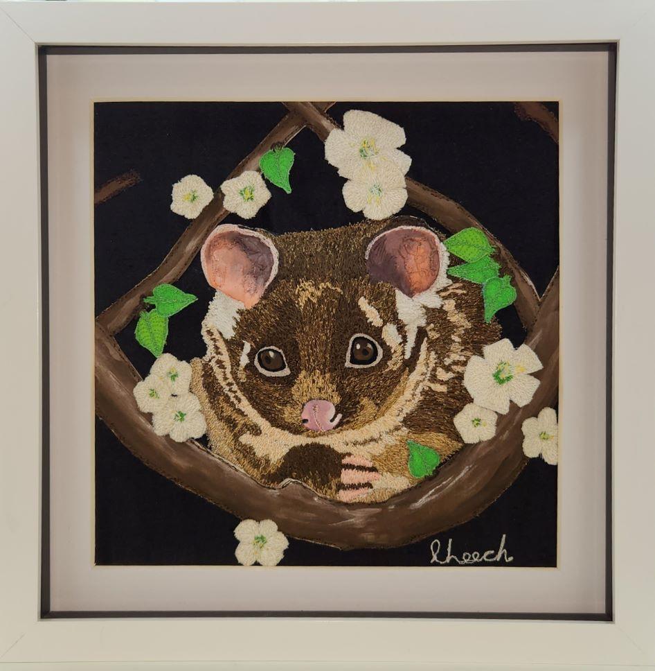 Hand embroidered image of a ringtail possum looking at the viewer