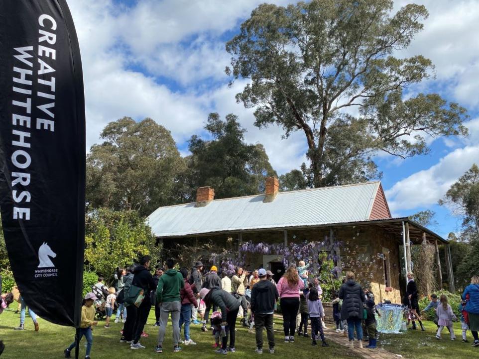 Crowd of visitors outside a stone cottage, bubbles blowing.