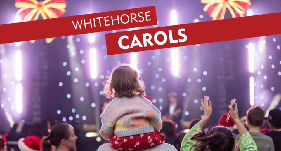 young girl sitting on parents shoulder watching outdoor stage