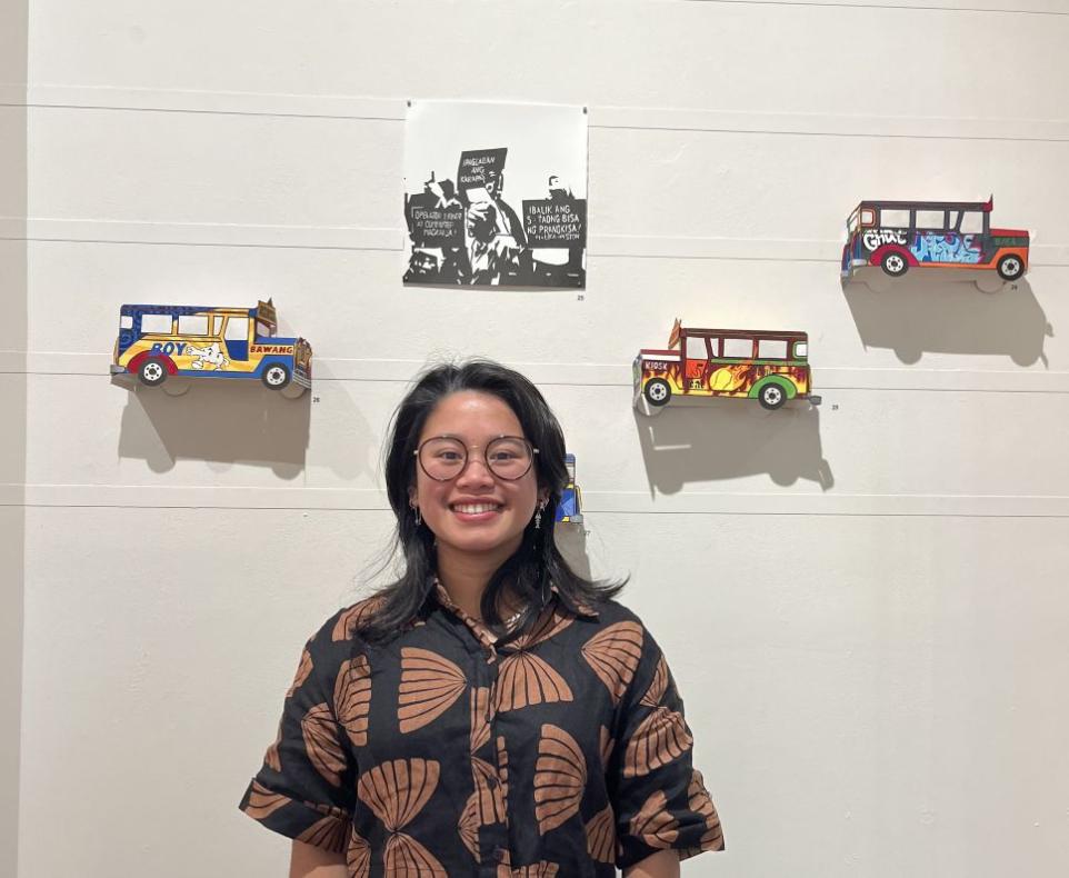 Photograph of an artist engaging the camera in front of a wall with their art