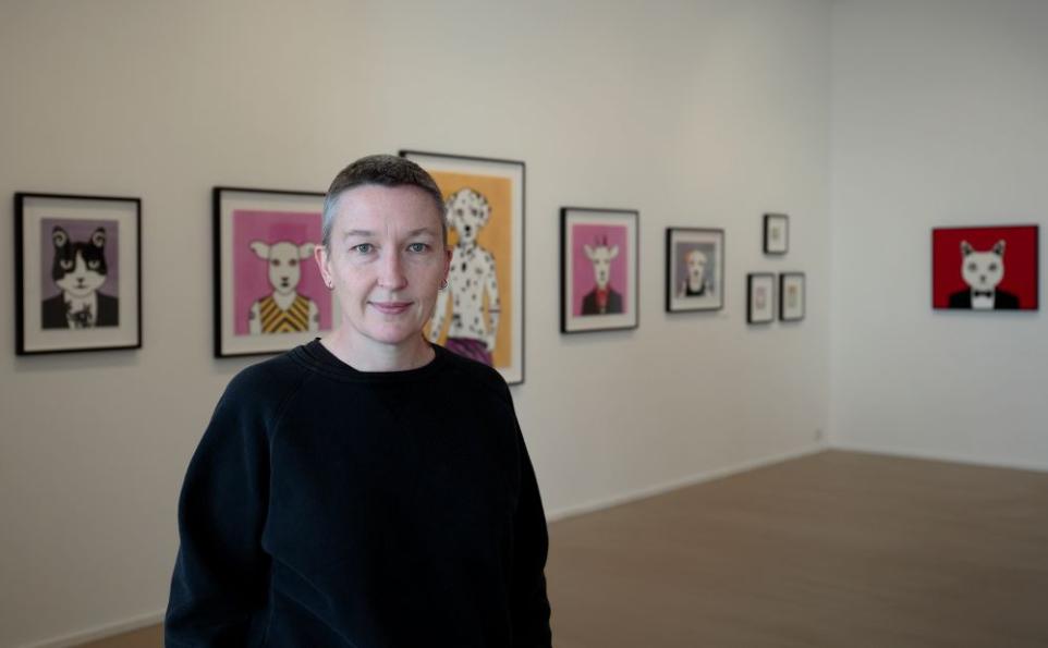 Artist Rona Green standing in a gallery with her prints on display.
