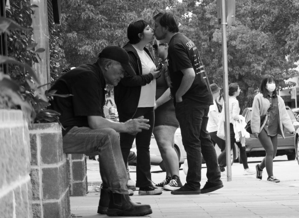 Black and white photo of a street scene, two people kissing.