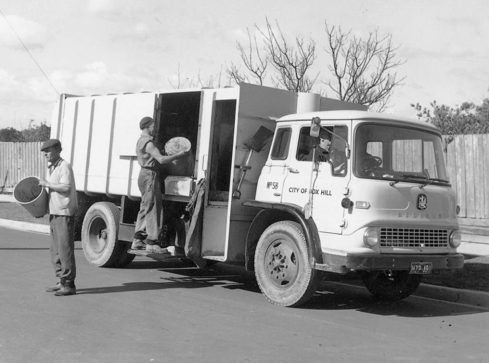 Black and white photograph showing a white truck and two garbage men.