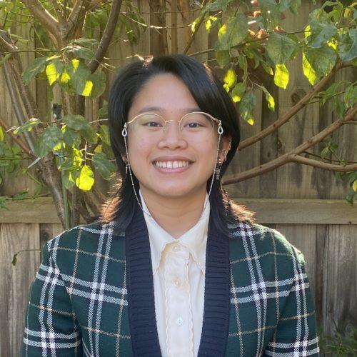 A lady with short black hair and clear glasses smiling at the camera