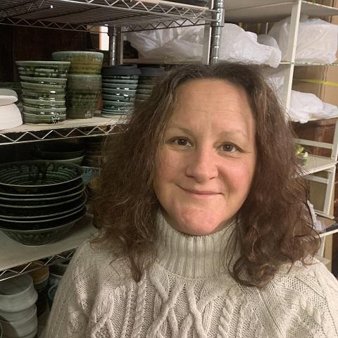 A lady with short brown hair in a white sweater smiling at the camera