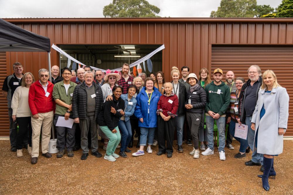 Large group of people in front of a shed.