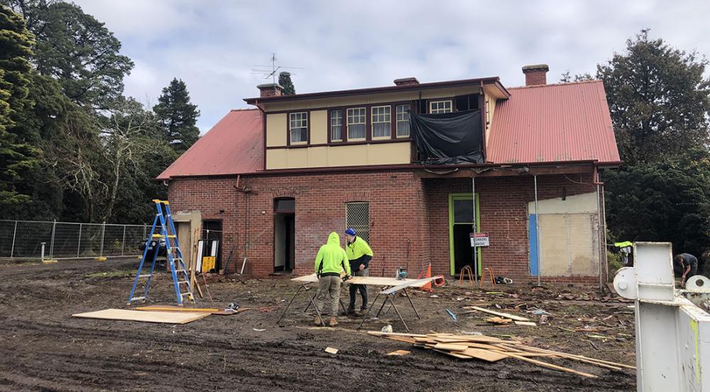 Construction workers cutting wood in front of a brick cottage