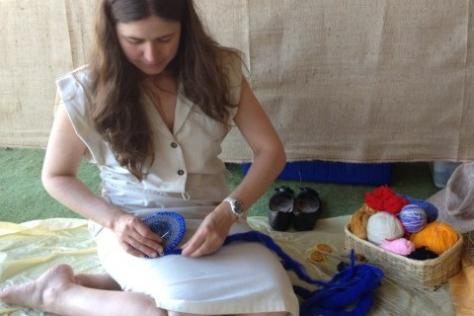 A women with long brown hair sitting on the floor weaving a basket with blue yarn