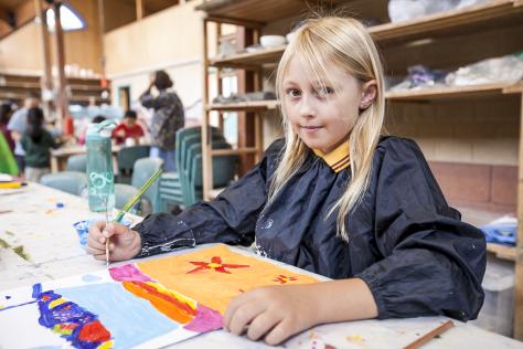 Child in visual arts class holding paint brush 