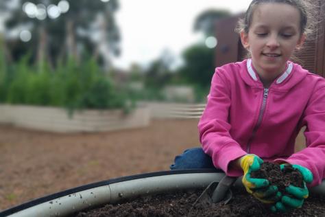 Image of a young girl picking up dirt from a planter box