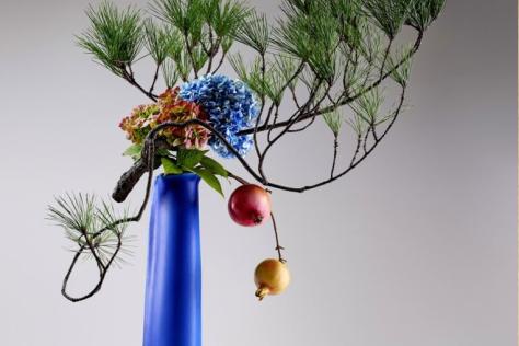 Arrangement of foliage, flowers and fruit in a slim electric blue vase