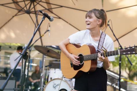 Young woman playing a guitar under a marquee with microphones and drumkit