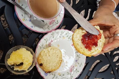 devonshire tea setting, person's hand putting Jam on scone