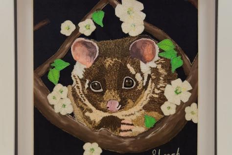 Hand embroidered image of a ringtail possum looking at the viewer