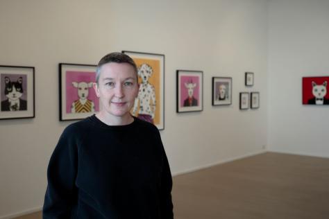Artist Rona Green standing in a gallery with her prints on display.