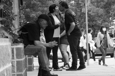 Black and white photo of a street scene, two people kissing.