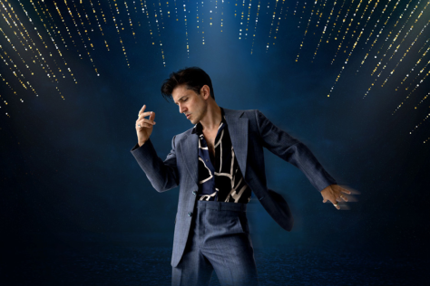 A man dressed in a dark suit poses like Elvis